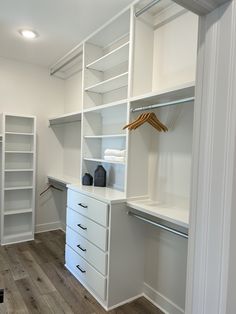 an empty walk in closet with white shelving and wooden flooring on the side