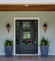 two planters on the front porch of a house with black doors and sidelights