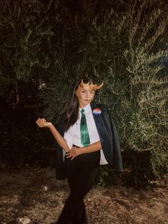 a woman in a suit and tie with horns on her head standing next to bushes