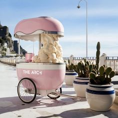 a pink ice cream cart sitting next to two potted cacti