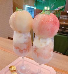 two glasses with ice cream and an apple on top, sitting on a pink tray