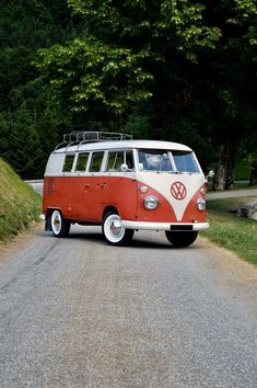 an orange and white vw bus driving down a road with trees in the background