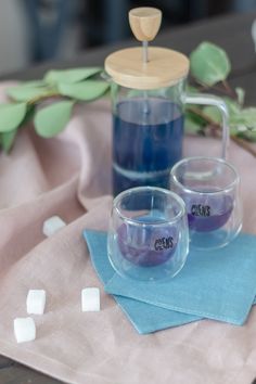 two glasses with blue liquid sitting on top of a cloth