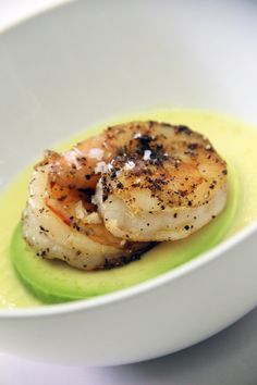 a white plate topped with shrimp on top of a green sauce covered in seasoning