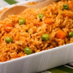 rice and peas in a white dish on a green tablecloth with a wooden spoon