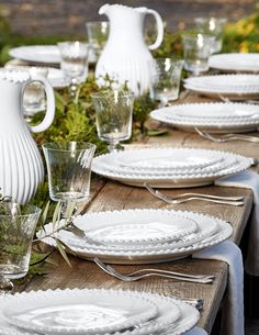 a long table with white plates and vases set on top of each other for an outdoor dinner