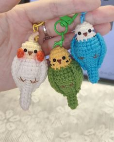 three small crocheted birds are being held in someone's hand while wearing key chains