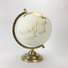 a white and gold globe with writing on the front is sitting on a metal stand