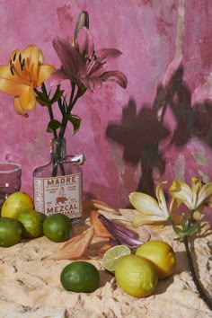 some lemons, limes and flowers are sitting on a table next to a pink wall