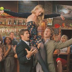 a woman is being lifted by two men in front of a bar full of people