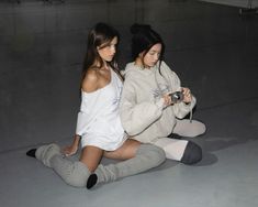 two young women sitting on the floor looking at their cell phones while they both wear matching outfits