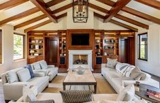 a living room filled with white couches and wooden ceiling beams in front of a fire place