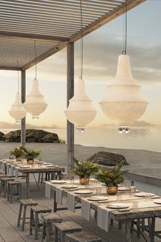 an outdoor dining area with wooden tables and hanging lights over the water at sunset or dawn