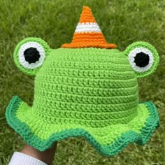 a crocheted frog hat is held up in the grass