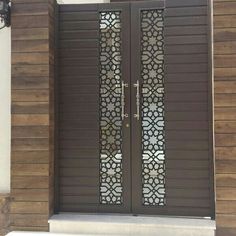 two brown doors with decorative glass on the side of a building in front of a white wall