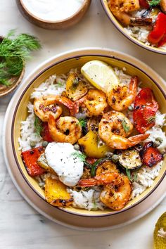 two bowls filled with shrimp and rice on top of a white table next to lemon wedges