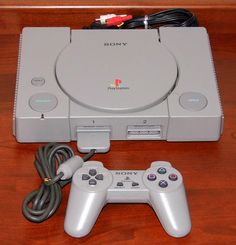 two video game controllers sitting next to each other on top of a wooden table with wires plugged in