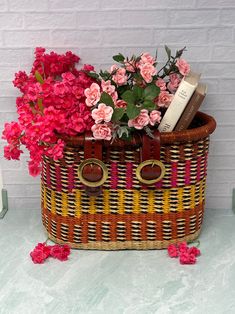 a basket filled with flowers and books on top of a white table next to a brick wall