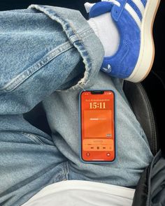 an orange and blue cell phone sitting on someone's lap with their legs crossed