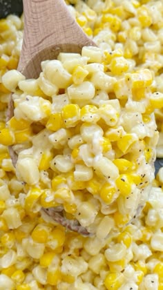 a wooden spoon filled with corn on top of a table next to other food items