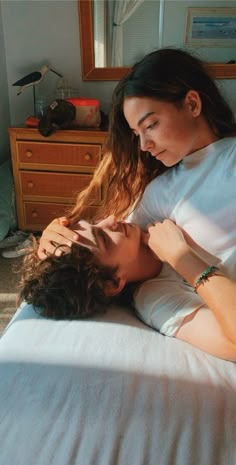 two people laying on a bed together in a room with sunlight coming through the window