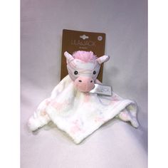 a stuffed cow with pink hair is laying on a white blanket that has a tag attached to it