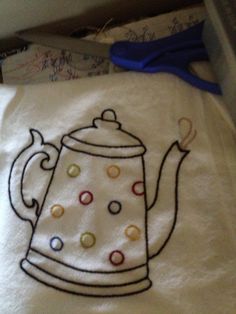 an embroidered tea pot on a white towel