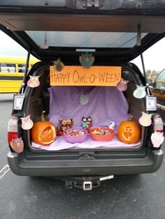 the back end of a vehicle with halloween decorations in the trunk and an orange sign that says happy owl - o - ween