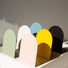 an assortment of different colored paper shapes on display in a white box with shadow from the wall behind it