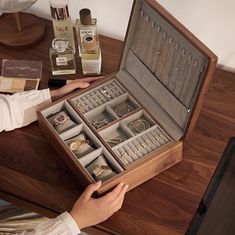 a person holding an open wooden box with jewelry in it on a table next to other items