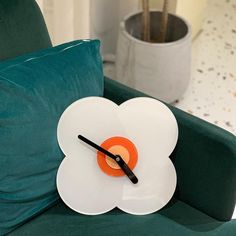 a clock made to look like an orange and white flower on a green chair in front of a potted plant