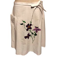 a white skirt with purple flowers painted on the side and tied at the waist,