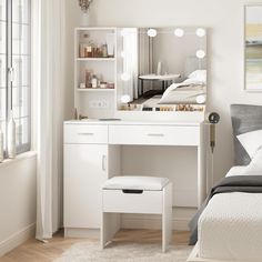 a bedroom with a white vanity table and stool next to a bed in front of a window