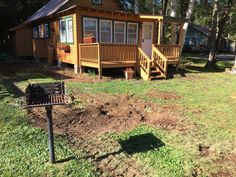 a small wooden cabin in the woods with a grill on the front lawn and steps leading up to it