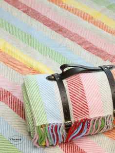 a multicolored striped blanket with leather straps on the bottom and an open suitcase sitting on top