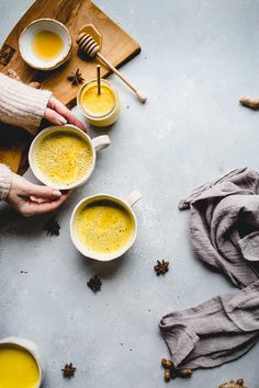 two hands holding mugs filled with yellow liquid