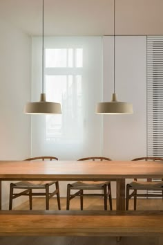 a wooden table with four chairs and two lamps hanging from it's sides in front of a window