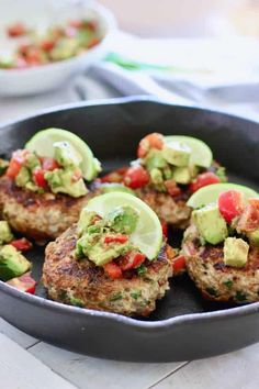 some meat patties with avocado and tomatoes in a skillet