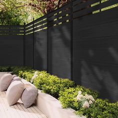 an outdoor seating area with pillows and flowers on the ground next to a wooden fence