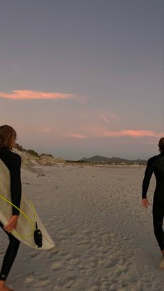 two people in wetsuits carrying surfboards on the beach