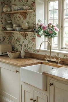 a white kitchen sink sitting under a window next to a wooden counter top with flowers on it