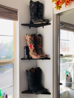 three black shelves with cowboy boots on them next to a sink and window in a bathroom