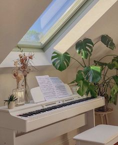 a white piano sitting under a window next to a potted plant