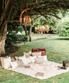 an outdoor seating area with pillows and chandelier hanging from the tree over it