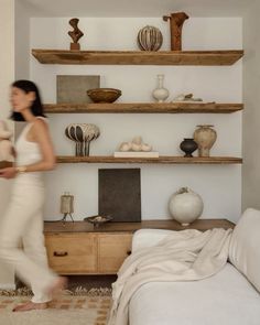 a woman is walking in front of shelves with vases and other items on them