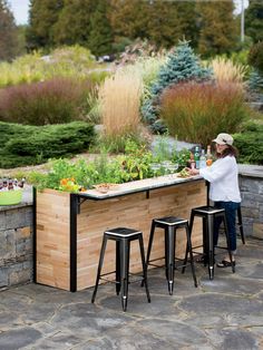 an outdoor bar with several stools and plants growing on the counter top, in front of a stone wall