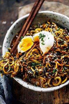 a bowl filled with noodles, eggs and chopsticks on top of a wooden table