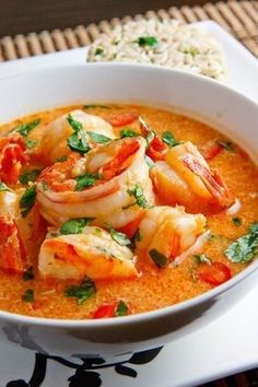 a white bowl filled with shrimp and tomato soup on top of a table next to rice