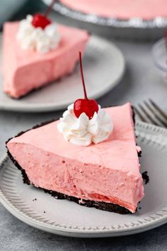 a slice of pink cheesecake with whipped cream and cherries on top is sitting on a plate