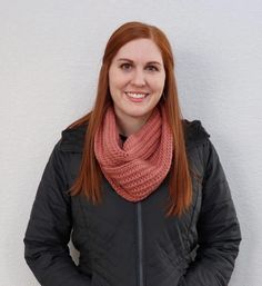 a woman standing in front of a white wall wearing a black jacket and pink scarf